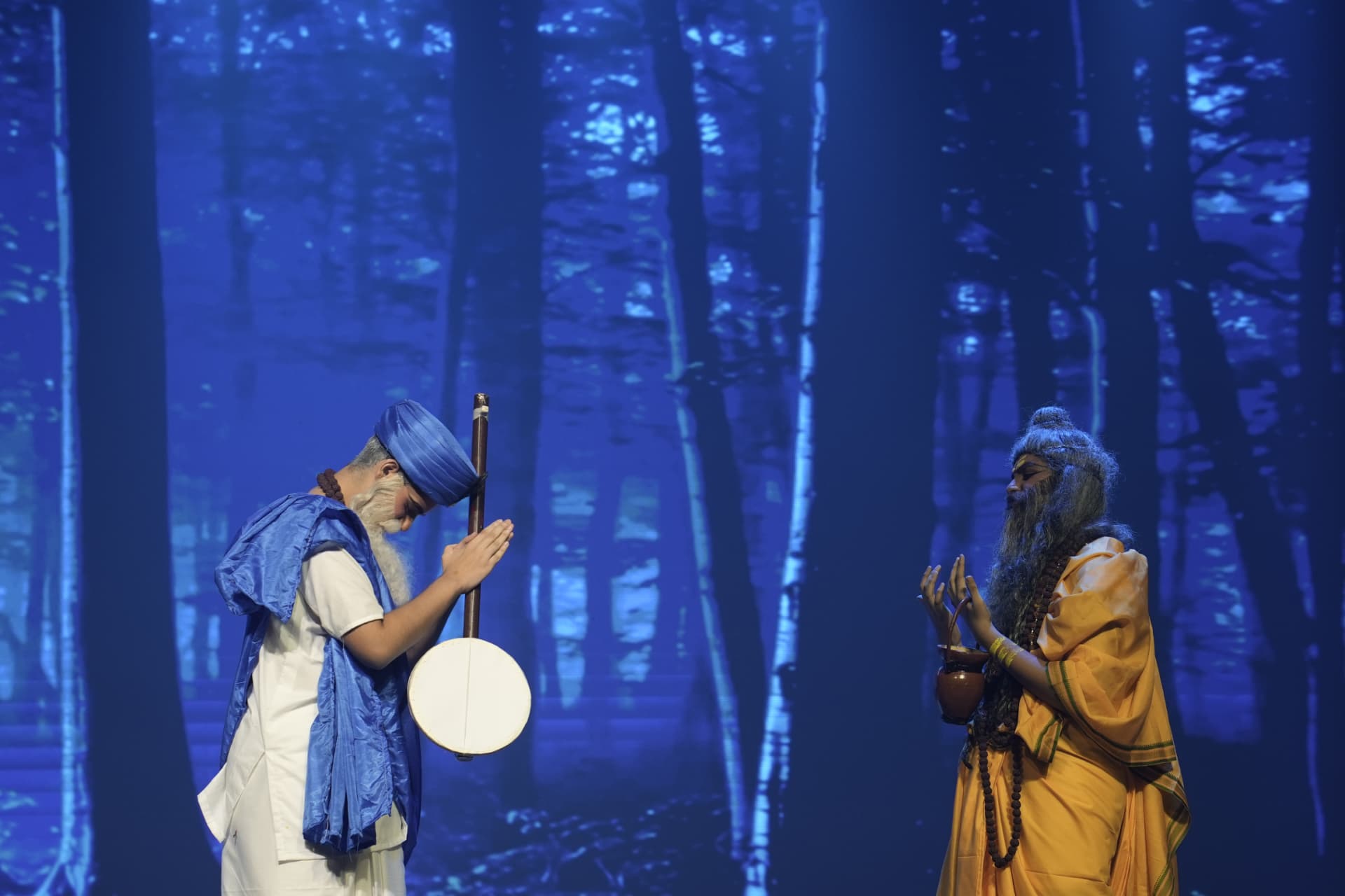 Two student actors performing a devotional drama scene against a forest LED backdrop